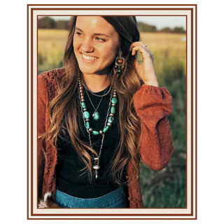 Woman with long hair and layered necklaces standing in a field | About Us | Texanna Belles